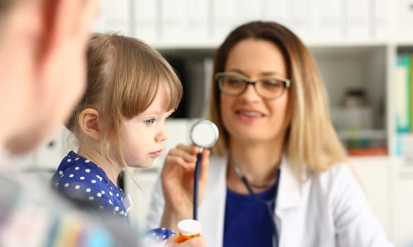 Woman doctor holding stethoscope near little girl. Pediatrics concept