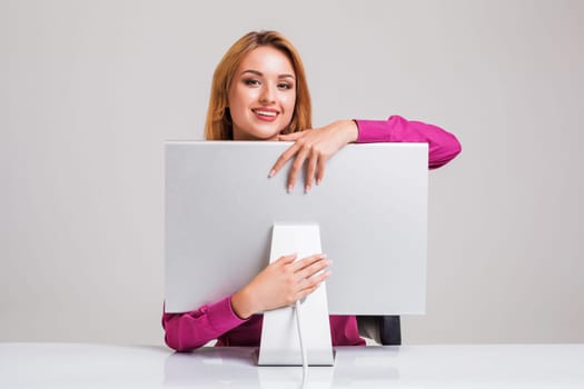 young woman sitting in the table and using computer on gray background. satisfied smiling girl hugging Monitor