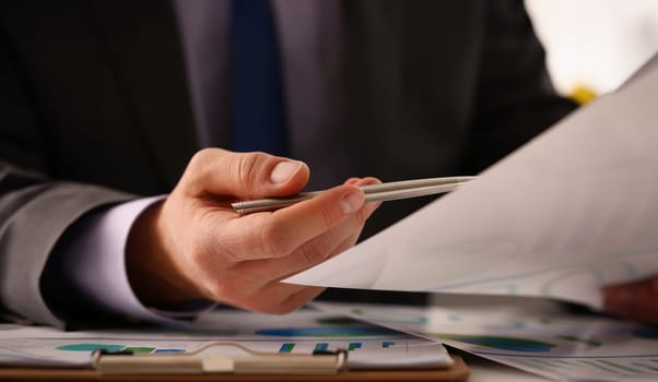 Male hand in suit hold siver pen in office with clipboard on table closeup. Comprehensive audit of enterprise business at all stages development.