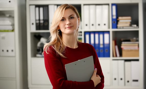 Happy smiling blond businesswoman holdig gray folder in hand office workplace look at camera