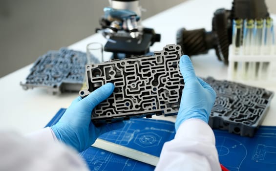 The auto repair service repairman in automatic gearboxes holds in his hand in blue protective gloves the hydroblock detail dehydrates the diagnostics and estimates detail test transmission closeup.