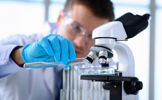 Male chemist holds test tube of glass in hand portrait overflows liquid solution potassium permanganate conducts an analysis reaction takes various versions of reagents using chemical manufacturing.