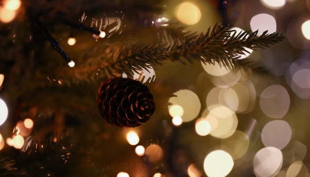 Pine cone hanging on christmas tree with lanterns bokeh background