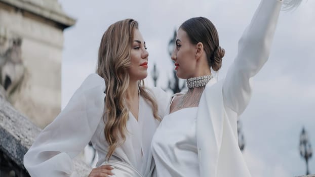 Two beautiful women blondes with red lips posing outdoors. Action. Adult ladies in white clothes holding a hat made of feathers, concept of fashion