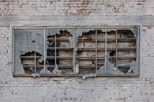 old window covered with torn ruberoid material and old wooden planks on white brick wall of an abandoned building, full-frame background and texture