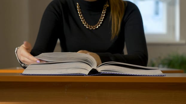 Women's hands leafing through a book. Woman sitting at the table leafing through the book.