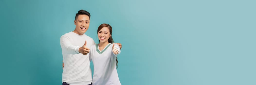 Photo of happy excited young loving couple standing isolated, showing thumbs up gesture.