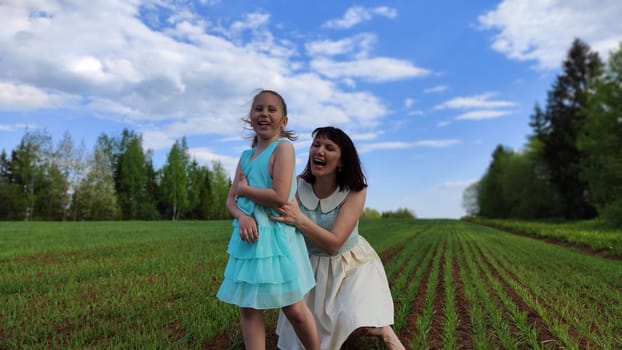 Happy mother and daughter enjoying rest, playing and fun on nature in green field. Woman and girl resting outdoors in summer or spring day