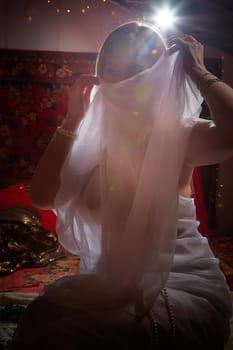 Beautiful European girl looking like Arab woman in red room with rich fabrics and carpets in sultan harem. Photo shoot of an oriental style odalisque. A model poses in sari as indian woman in india