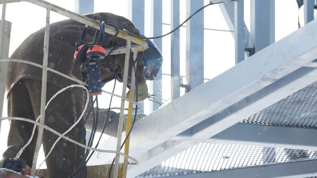 welder working with electrode at arc welding in construction site winter outdoors. Welder protective mask works outdoors in winter close up.