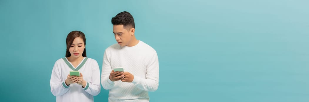 Asian young man spying at girlfriend text messaging through smartphone