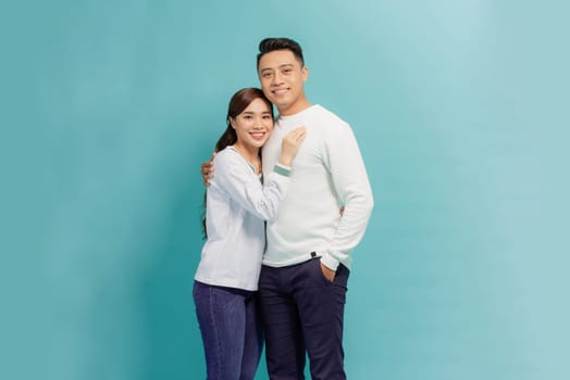 A happy young asian couple hugging while standing together and looking at camera