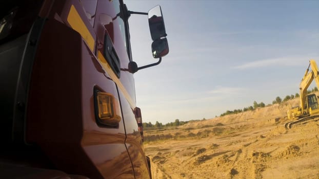 View from a wheel of the off-road truck riding in a dirt road on cloudy sky background. Close up for red cab of a lorry moving on the country, dusty road in a summer, sunny day.