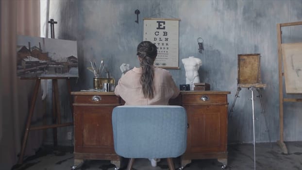 Businesswoman typing something on laptop and sitting at the desk, rear view. Back view of brunette woman sitting in the art workshop.