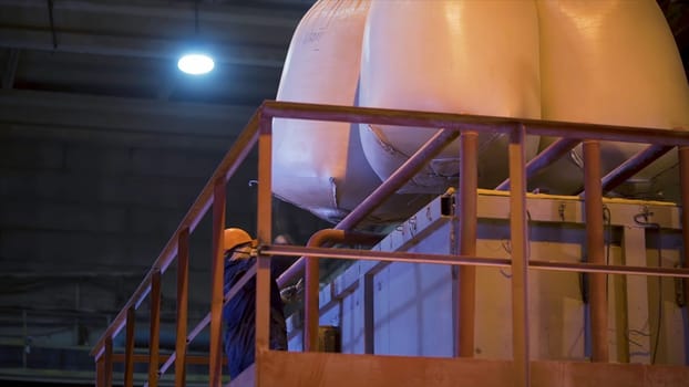 Worker at factory with bags for raw materials. Stock footage. Worker in hard hat opens suspended bags filled with raw materials for mixing in industrial equipment.