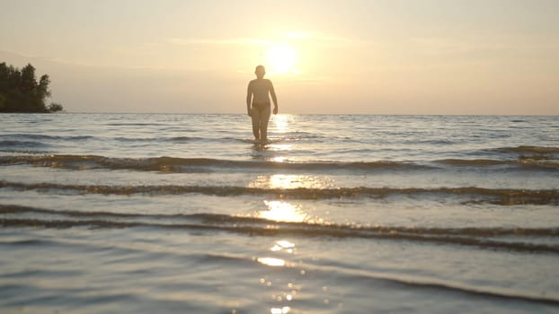 Silhouette of man walking in water on sunset background. Creative. Man comes out of water on background of sunset. Man comes out of water at sunset.
