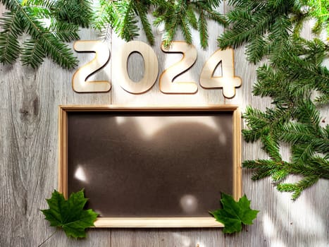 Wooden figures and numbers of the new year 2024 with frame and fir branches of Christmas tree. Celebration. Abstract background, pattern, frame, place for text, copy space