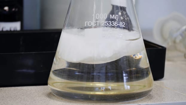 Laboratory glass Erlenmeyer conical flask filled with chemical white liquid for a chemistry experiment in a science research lab.