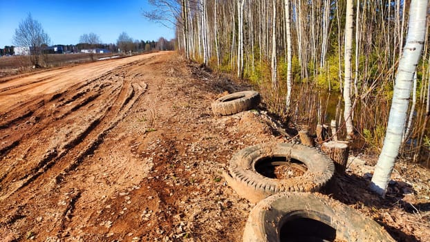 Old rubber tires from car wheels are thrown into the mud on road. The concept of environmental pollution. Garbage from human activities