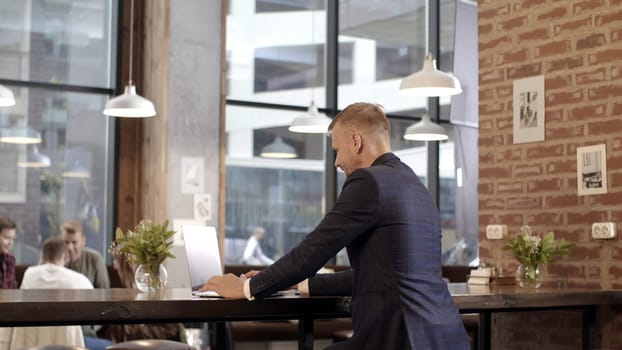 Rear view of businessman working at table in cafe. Stock footage. Businessman works at laptop even during lunch break in cafe.