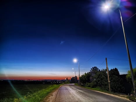 Asphalt road at night with lanterns on the side of road and the natural landscape around