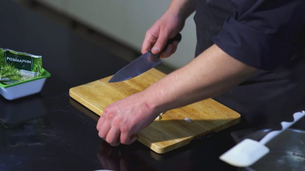 The cook cuts the onion. ART. Man in the kitchen cuts white onion into half rings with knife. Next to the board is spatula and bag of rosemary.