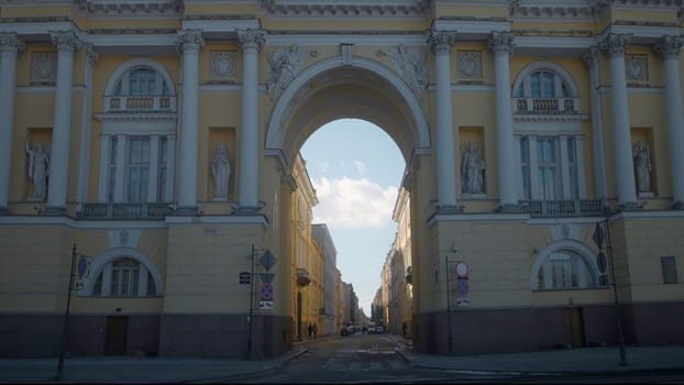 Beautiful view of street through ancient arch. Action. Ancient architectural arch overlooking street on sunny day. People walk along street with old arch.