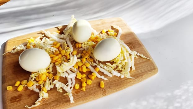 Chopped Peking cabbage, peeled eggs and yellow canned corn on cutting board as background. Cooking a healthy eco-friendly salad from natural products. Copy space and place for text