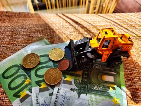 A small toy tractor or excavator on bundle of money. The concept of the high cost of technology. The possibility of earning money with construction machinery