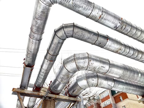 Metal pipes in thermal insulation winding outdoors and the over-illuminated white sky on background