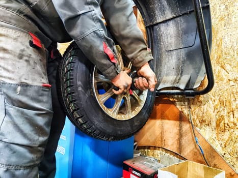 Ishim, Russia - November 27, 2023: Mechanic repairs a car wheel and makes a tire in a dirty garage. Replacement of summer wheels, tires for winter indoors