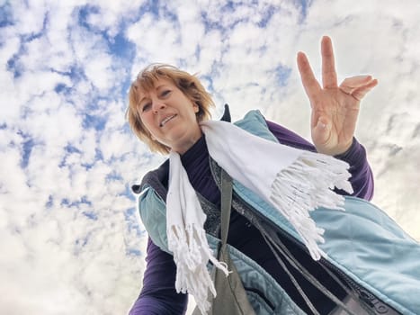 Happy, funny, funny adult girl takes a selfie against a blue sky with white clouds. A middle-aged woman poses on the phone in nature in autumn or spring