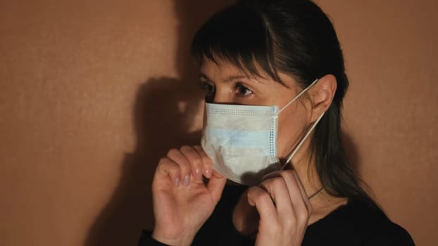 Woman putting on blue medical mask, side view. Middle aged woman wearing disposable medical face mask for protection against coronavirus, COVID 19.
