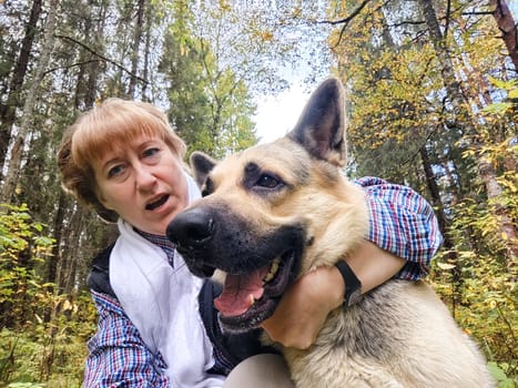 Adult girl with shepherd dog taking selfies in forest. Middle aged woman and big shepherd dog on nature. Friendship, love, communication, fun, hugs