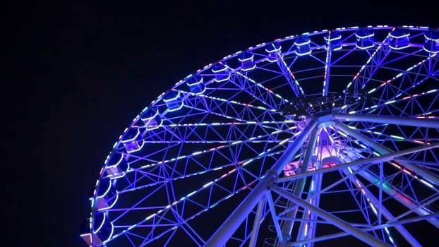 Ferris wheel in blue neon light on dark background, Part of Ferris wheel with blue illumination against a black sky background at night. Ferris wheel by night. Ferris wheel with multi-colored illumination against the dark blue night sky. Ferris wheel and assorted Carnival
