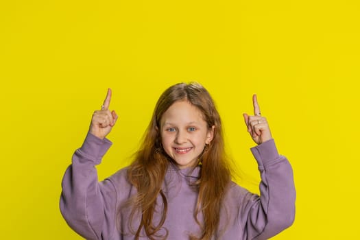 Happy cute girl showing thumbs up pointing empty place up, advertising area for commercial text, copy space for goods promotion banner, copy-space. Young child kid. Studio shot on yellow background