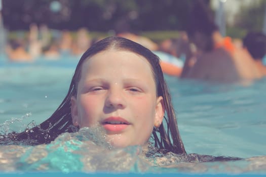 A picture of a little girl at a swimming pool in summer. A small girl swimming to the edge of a swimming pool at a swimming pool. Concept of summer, water fun, sun and relaxation.