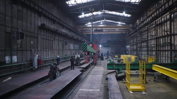 Metal beam is moved on chains in factory. Clip. Steel beam suspended on chains is dragged at factory. Suspended beam on chains moves around factory.