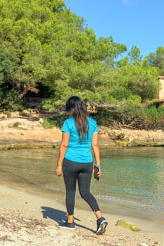 latina woman in sportswear walking and listening to music with her smart phone on the beach,