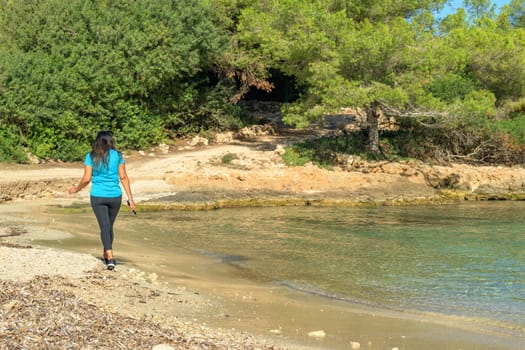 Latina sportswoman, walking along the shore of a Mediterranean island beach,