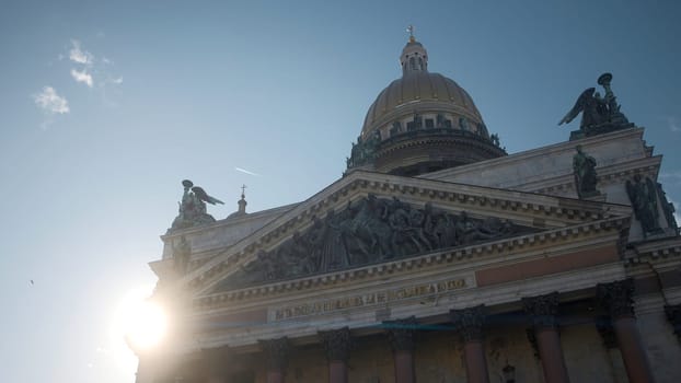 View from below of ancient cathedral with statues and dome. Action. Beautiful old cathedral on background of bright sun and blue sky. Dome and statues in architecture of ancient cathedral.
