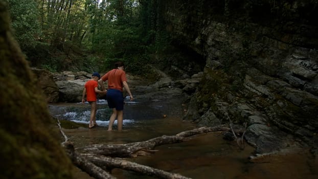 Boy and mother walking among rocks in cold stream. Creative. Hiking in wild nature