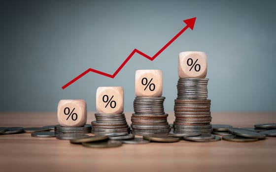 Percent sign on a wooden cube with row of coins in idea for FED consider interest rate hike, inflation concept, red graph arrow, world economics, and inflation control, Money and budget management
