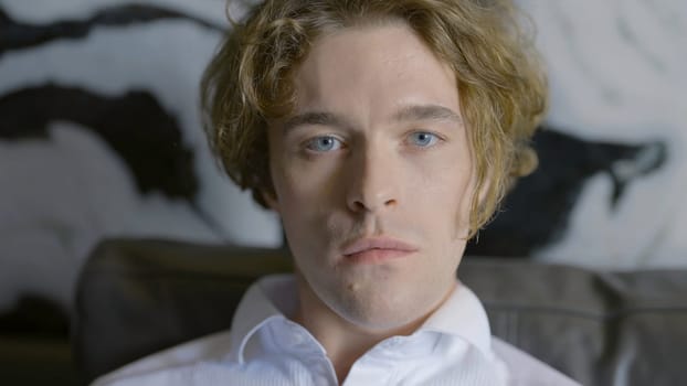 Handsome man in white shirt looks at camera. Action. Man looks emotionlessly into camera. Man looks at camera tensely or tiredly.