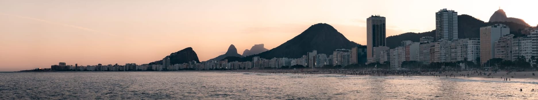 Twilight descends on Copacabana Beach, featuring modern skyline and Christ the Redeemer's iconic outline in Rio.