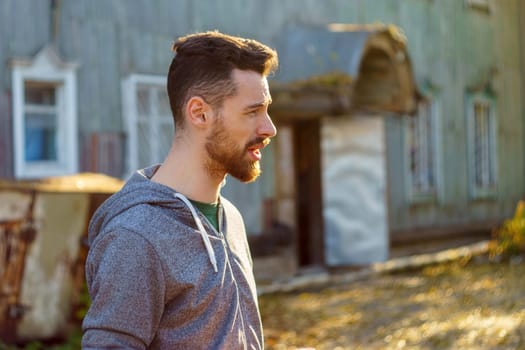 Brutal handsome man, aged, 30-35 years old, stands in the park in a gray sweatshirt