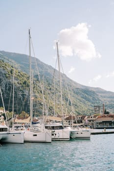 Sailing yachts are moored along the shore against the backdrop of green mountains. High quality photo