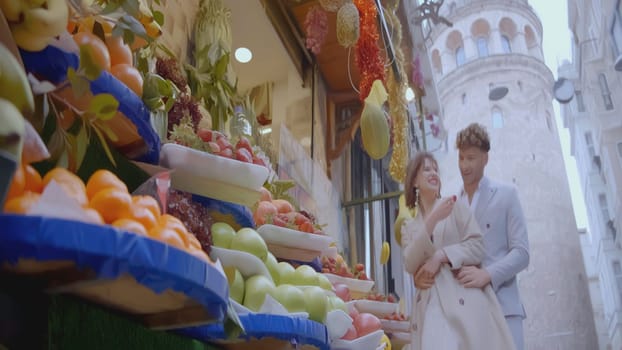 Happy newlyweds at market. Action. Beautiful couple of newlyweds at fruit shop. Newlyweds relax and laugh at European market on background with ancient archetype.