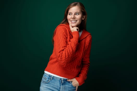 Cheerful young woman with brown hair dressed in a red knitted sweater on a green background.