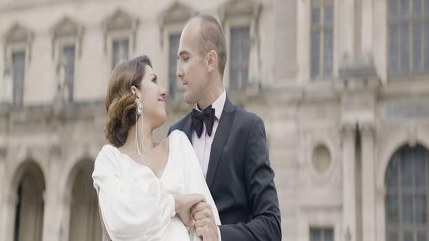 Newlyweds with an antique building on the background. Action. Beautiful bride and groom look each other and kiss